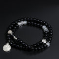 Tao Mountain Spirit Coin pendant with Yin-Yang engraving on double-loop black obsidian bracelet, displayed on zen stone slab