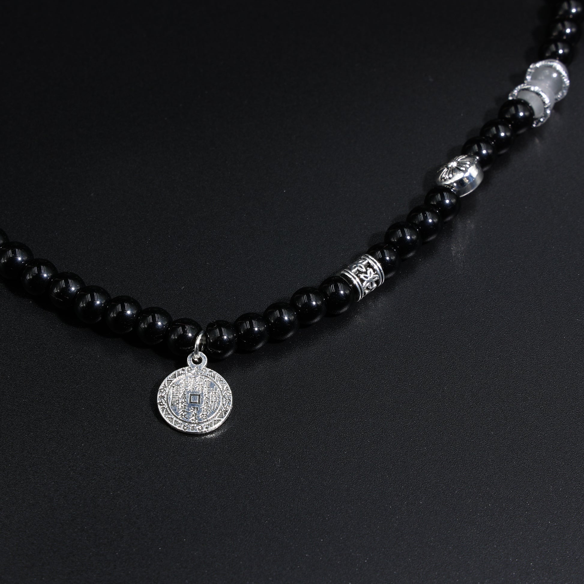 Tao Mountain Spirit Coin pendant with Yin-Yang engraving on double-loop black obsidian bracelet, displayed on zen stone slab