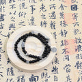 Tao Mountain Spirit Coin pendant with Yin-Yang engraving on double-loop black obsidian bracelet, displayed on zen stone slab